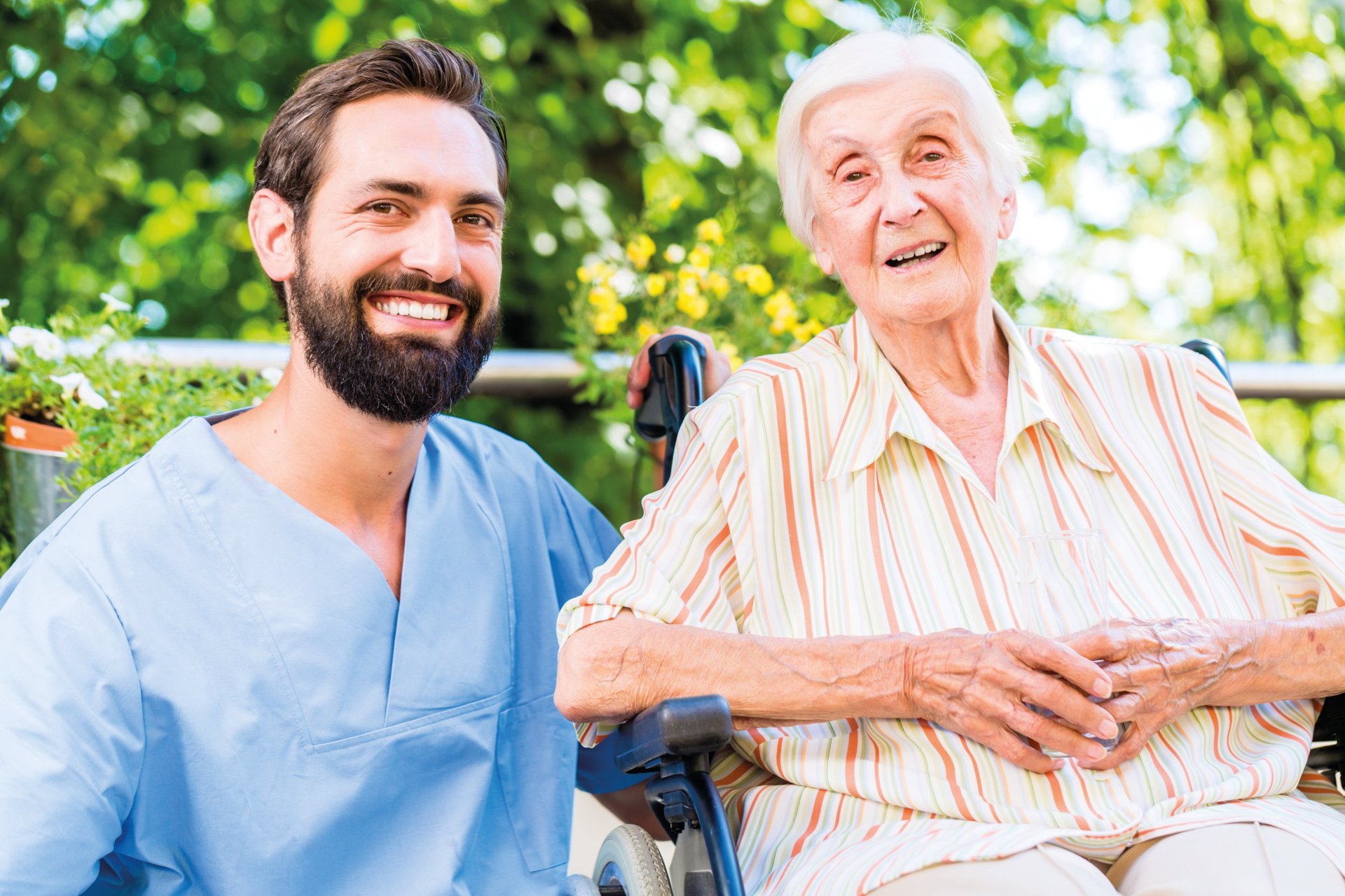 Ein Pflegefachmann sitzt mit einer Patientin im Grünen.