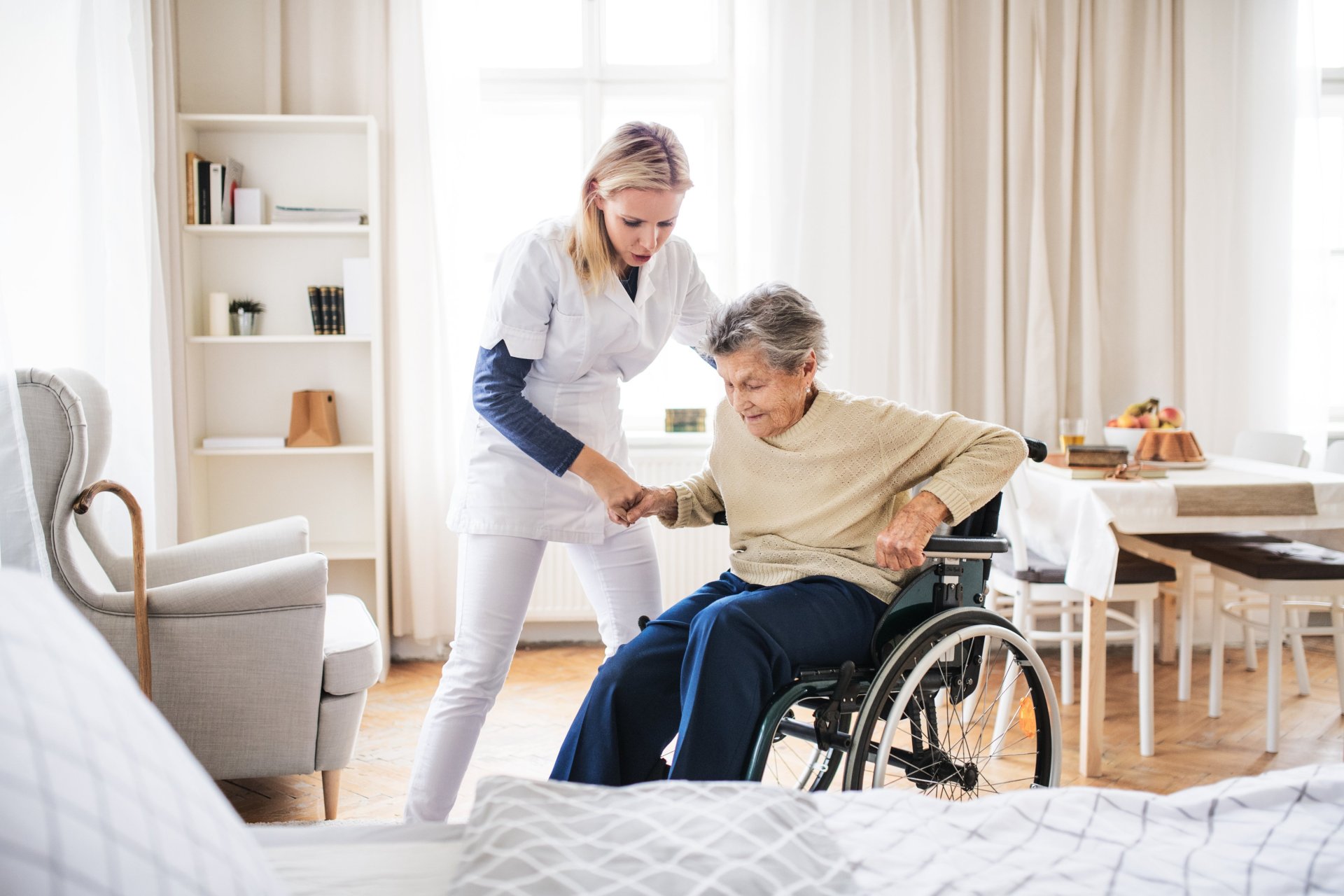 Eine Altenpflegehelferin kümmert sich um eine Patientin im Rollstuhl.