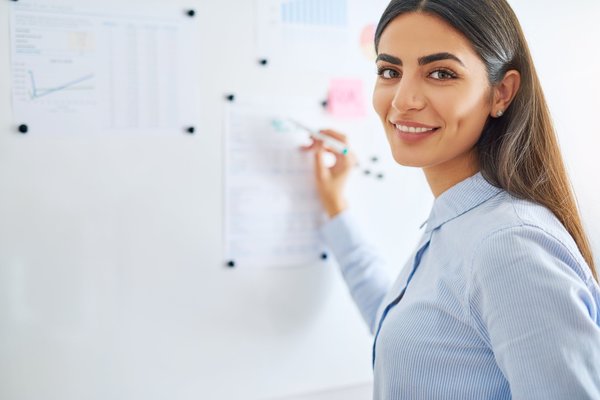 EIne junge Projektmanagerin steht an einem Whiteboard und notiert Abläufe. 