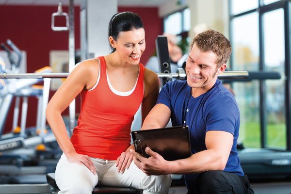 Ein Sport- und Fitnesskaufmann bespricht einen Trainingsplan mit einer Kundin in einem Fitnessstudio.