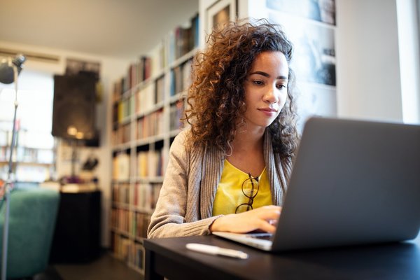 EIne junge Frau sitzt an einem Noteboook und lernt in einer Bibliothek.