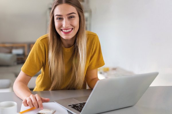 Eine junge Frau sitzt an ihrem Laptop und lächelt in die Kamera.