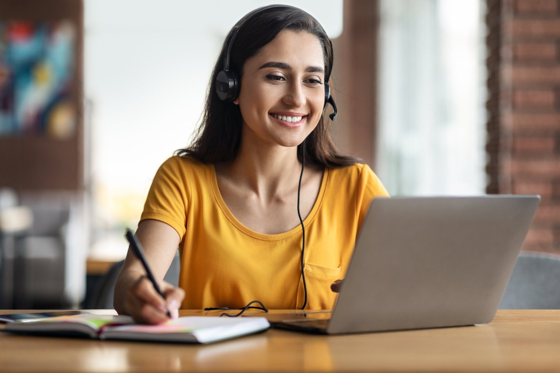 Eine junge Frau lernt am Laptop mit einem Headset auf dem Kopf.