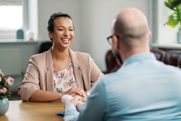 Eine Frau sitzt in einem individuellen Coaching ihrem Coach gegenüber und lacht.