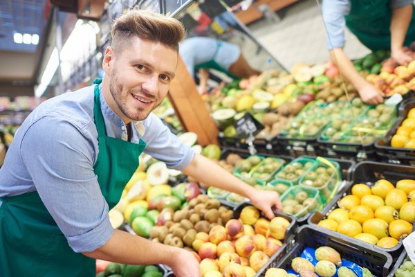 Ein Verkäufer räumt Obst und Gemüse in einem Supermarkt in die Auslage.