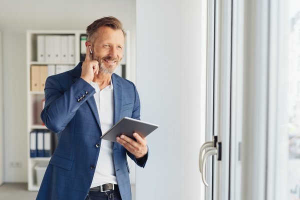 Ein Industriekaufmann steht in seinem Büro und hält ein Tablet in der Hand.