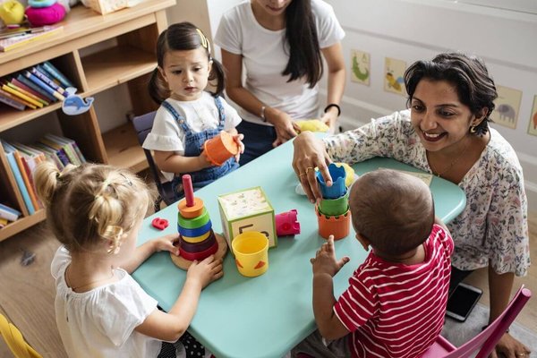 Eine Erzieherin mit Migrationshintergrund spielt mit Kindern in einer Kita.