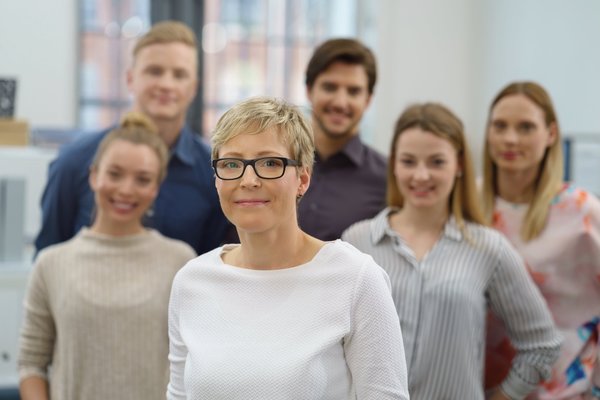 Eine Geschäftsführerin steht vor einer Gruppe Mitarbeitenden.