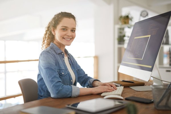 Eine medizinische Kodierfachkraft sitzt am Computer und lächelt in die Kamera.