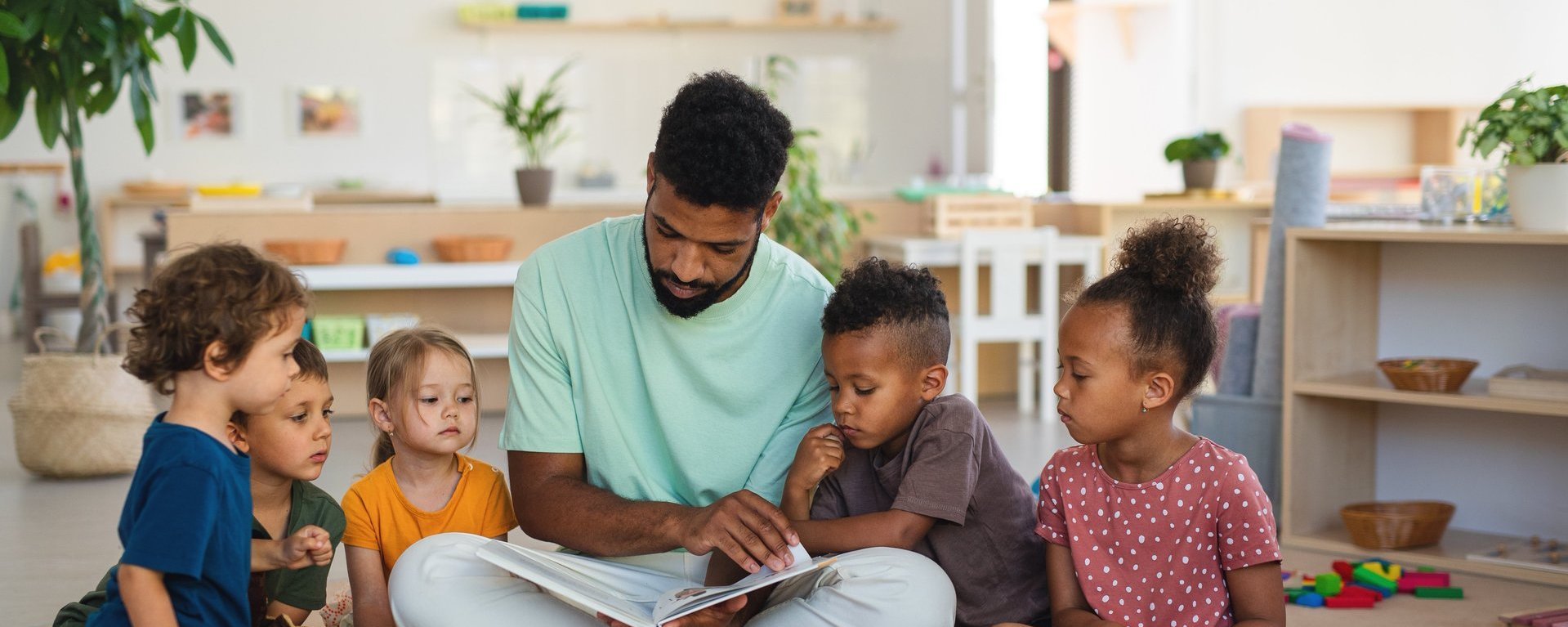 Ein Erzieher liest einigen Kindern in einem Kindergarten ein Buch vor.