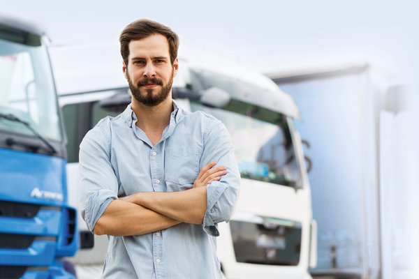 Ein Kaufmann für Logistik und Speditionsdienstleistungen steht vor einem LKW-Fuhrpark.